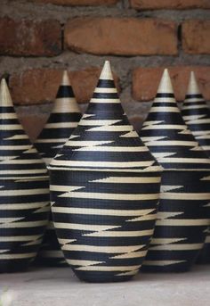 four black and white vases sitting on a table next to a brick wall in front of a brick wall