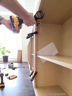 a man is using a drill to attach shelves in a room with tools on the floor