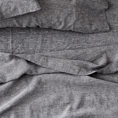 an unmade bed with grey sheets and pillows