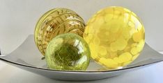 two yellow and one green glass vases in a silver bowl on a white table