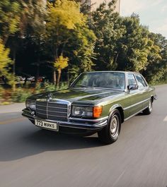 a green mercedes benz parked on the side of the road with trees in the background