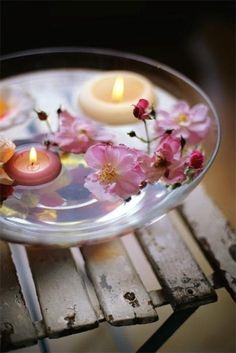 two candles and some pink flowers in a glass bowl