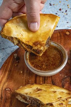 a person dipping some food into a bowl on top of a wooden tray with other foods