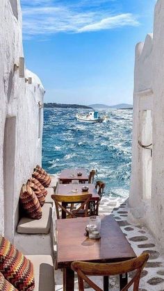 an outdoor seating area with tables and chairs on the beach next to the ocean in front of whitewashed buildings