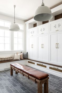 a bench sitting in the middle of a room next to white cupboards and windows