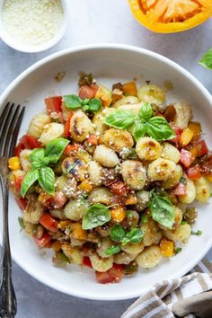 a white bowl filled with pasta and vegetables next to two bowls of seasoning on the side