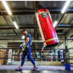 a man in blue shirt and yellow gloves standing next to a red boxing punching bag