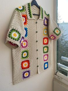 a crocheted shirt hanging on a wall next to a window