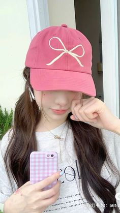 a girl wearing a pink hat is looking at her cell phone and holding it up to her face