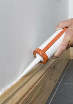 a person is holding an orange and white roller on the wall next to a tile floor