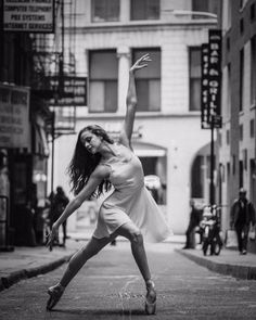 a black and white photo of a woman dancing on the sidewalk in an urban setting