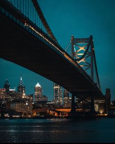 the city skyline is lit up at night, as seen from across the water with a bridge in the foreground