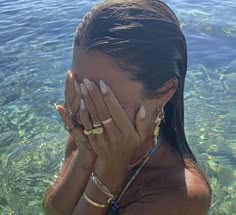 a woman covers her face with her hands in the clear blue water, while standing in shallow water