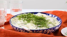 a blue and white bowl filled with food on top of a red cloth next to two glasses