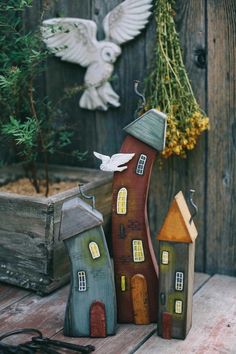 two small wooden houses sitting next to each other on top of a wooden table near a potted plant