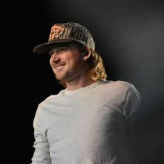 a man wearing a camo hat smiles at the camera while standing in front of a black background