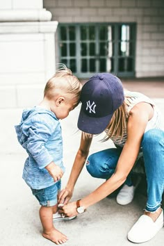 a woman kneeling down next to a little boy with a baseball cap on his head