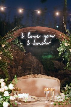 a table set up with flowers and greenery for a wedding reception in the evening