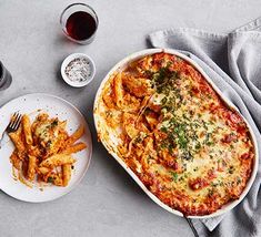 a white plate topped with cheesy pasta next to a bowl of french fries