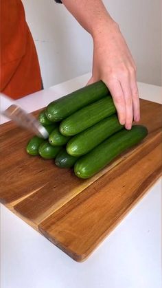 a person cutting up cucumbers on a wooden cutting board with a large knife