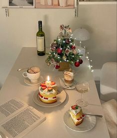 a table topped with two cakes next to a bottle of wine and an open book