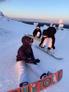 three snowboarders are sitting in the snow and one is holding his board up