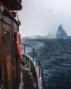 an iceberg is seen from the deck of a boat in the ocean as snow falls