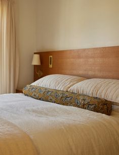 a bed with white sheets and pillows in a bedroom next to a window that has curtains on both sides