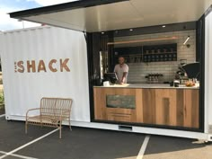 a man standing in the back of a food truck next to a table and chair