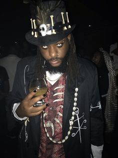 a man with dreadlocks and a top hat is holding a drink in his hand