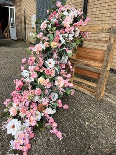 pink and white flowers on the ground next to a wooden bench in front of a brick building