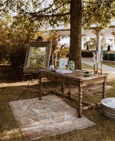 an old wooden table with a mirror and rug on the ground in front of it