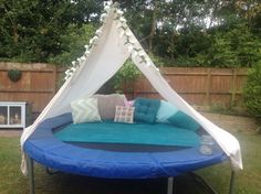 a blue and white bed with pillows on it in the grass next to a wooden fence