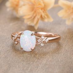 a white opal and diamond ring sitting on top of a table next to flowers