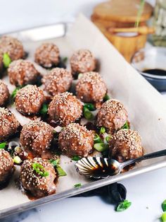 a tray filled with meatballs covered in sesame seeds and garnished with green onions