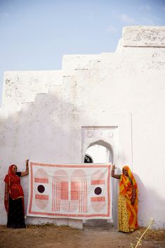 two women standing next to each other holding up a large orange and white piece of cloth