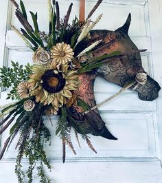 a horse head decorated with flowers and greenery hangs on a door handle in front of a white wall