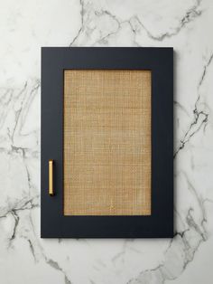 a black frame with a rattan pattern and a gold pen on the side, sitting on a marble surface