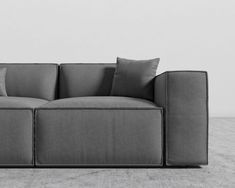 a gray couch with pillows on it in front of a white wall and concrete floor