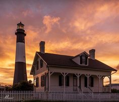 a white house with a black roof and a light tower in the background at sunset