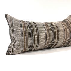 a striped pillow on a white surface with a black and brown stripe pattern in the middle