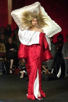 a woman walking down a runway in a red and white dress with an umbrella on her head