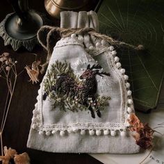 an embroidered bag with pine cones and berries on it sitting on a table next to other items