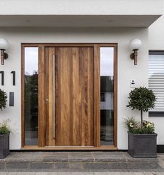 two planters with potted plants are in front of a modern wooden door on a white house