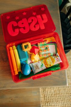 a red plastic container filled with toys on top of a wooden table