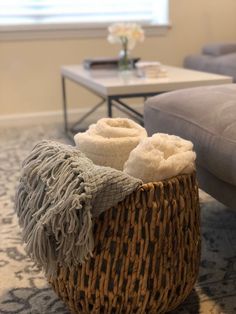 a wicker basket with two folded towels in it sitting on the floor next to a couch