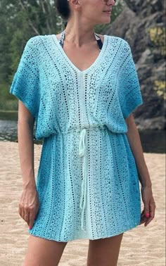 a woman standing on top of a sandy beach wearing a blue crochet dress