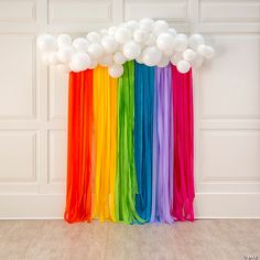 a rainbow colored curtain with white balloons hanging from it's sides in front of a wall