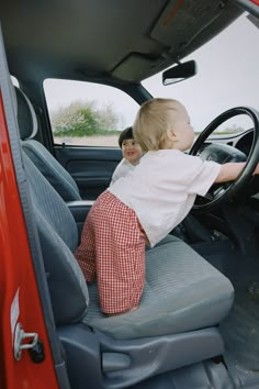 a little boy sitting in the driver's seat of a red truck with his hands on the steering wheel