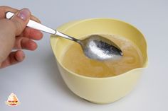 a person holding a spoon in a yellow bowl with liquid and sugar on the side